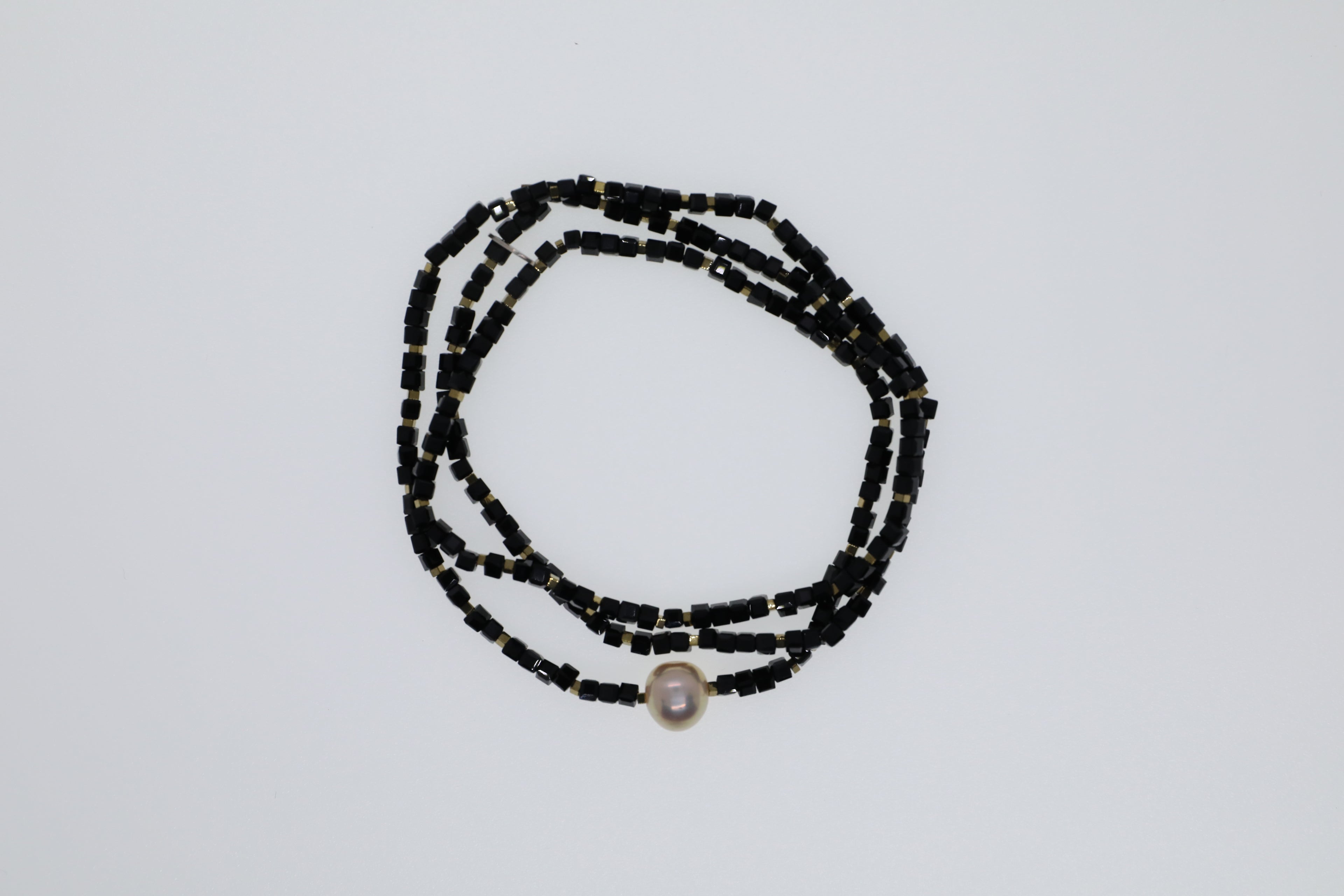 Goldfarbene Hämatitwürfel, schwarze Glasperlen und eine Süßwasserperle