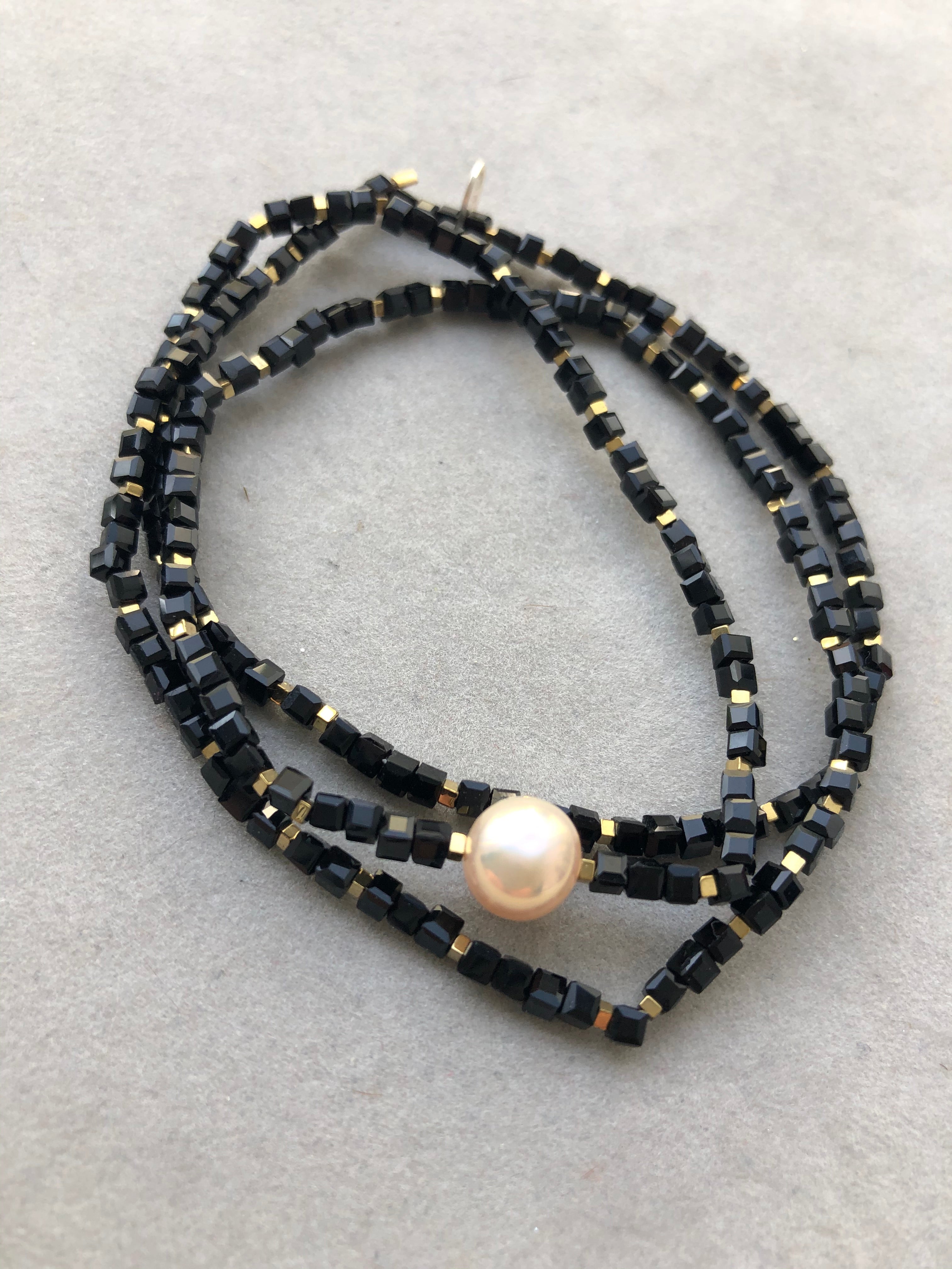 Goldfarbene Hämatitwürfel, schwarze Glasperlen und eine Süßwasserperle