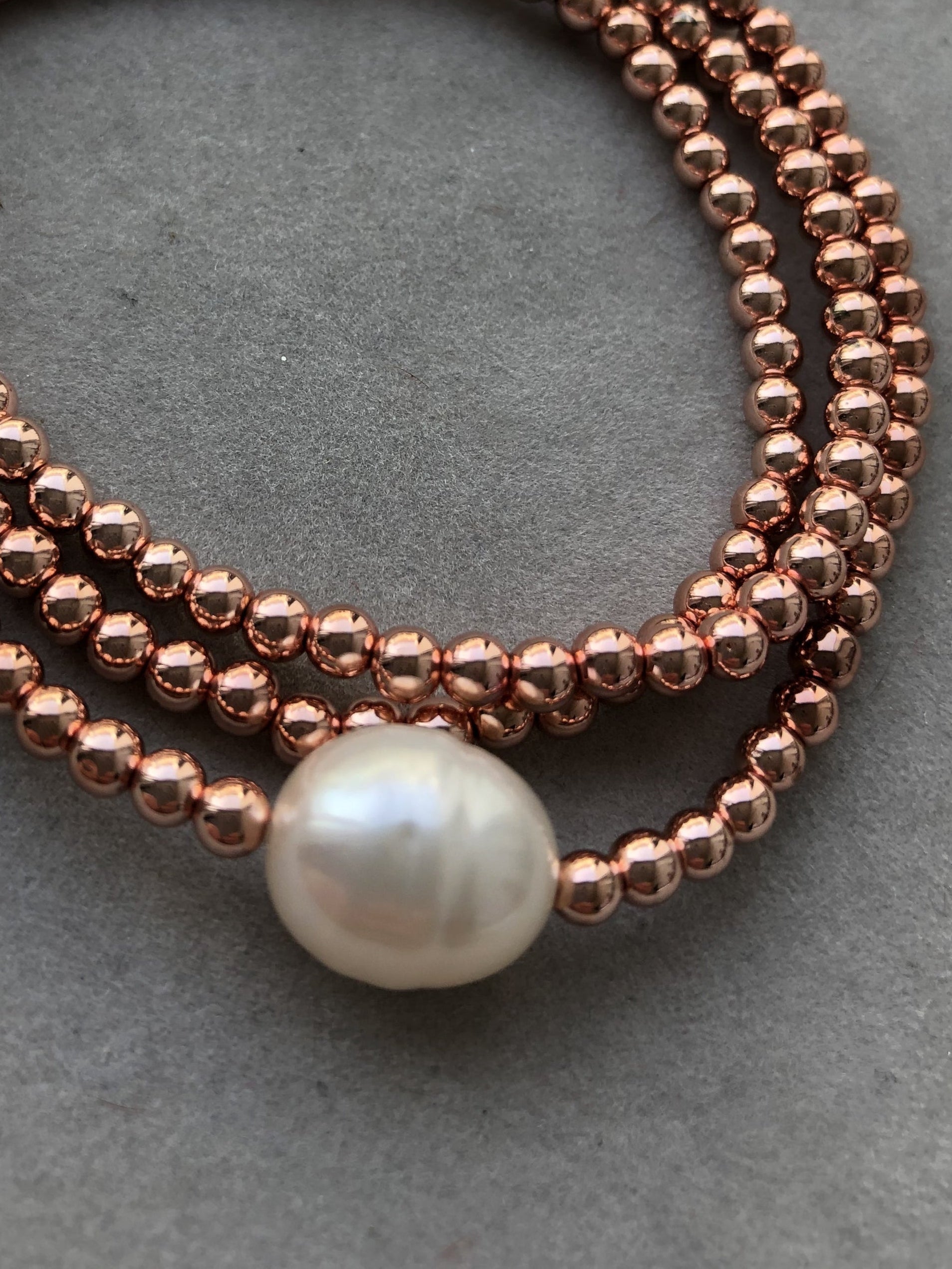 Kupferfarbene Hämatitkugeln und eine weiße Süßwasserperle