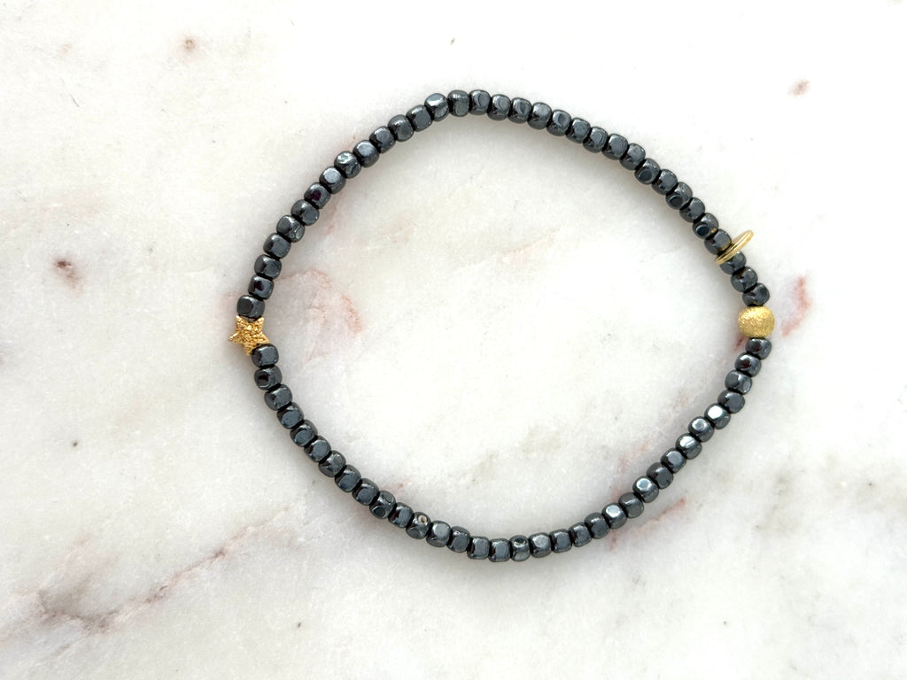 Armband aus anthrazitfarbenen Hämatitwürfeln und einem vergoldeten Stern aus Silber. Dazu eine vergoldete Silberkugel