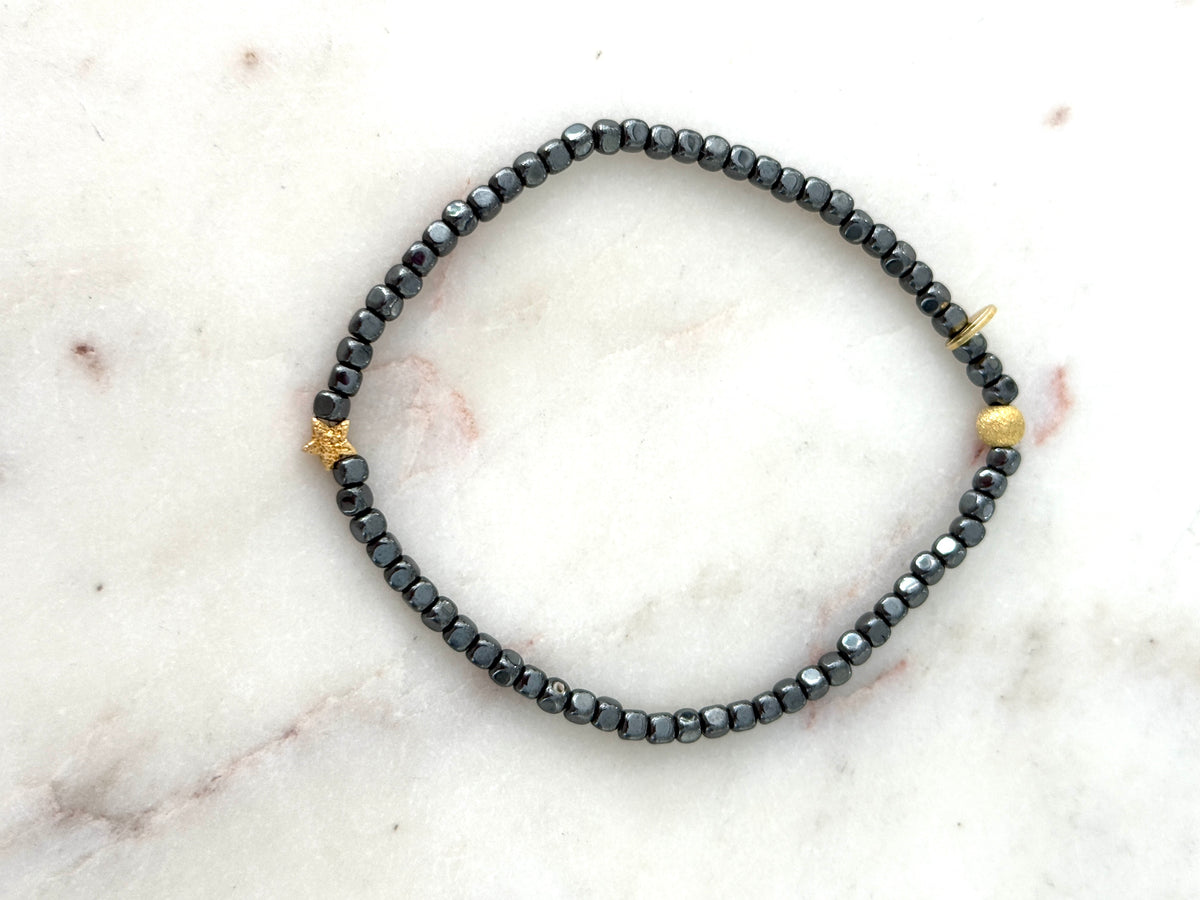 Armband aus anthrazitfarbenen Hämatitwürfeln und einem vergoldeten Stern aus Silber. Dazu eine vergoldete Silberkugel